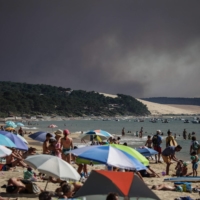 Beach-goers watch as a black cloud of smoke from a fire that hit La Teste-de-Buch forest rises from the Pyla Dune in the background, in the Arcachon basin in France on Wednesday. | AFP-JIJI