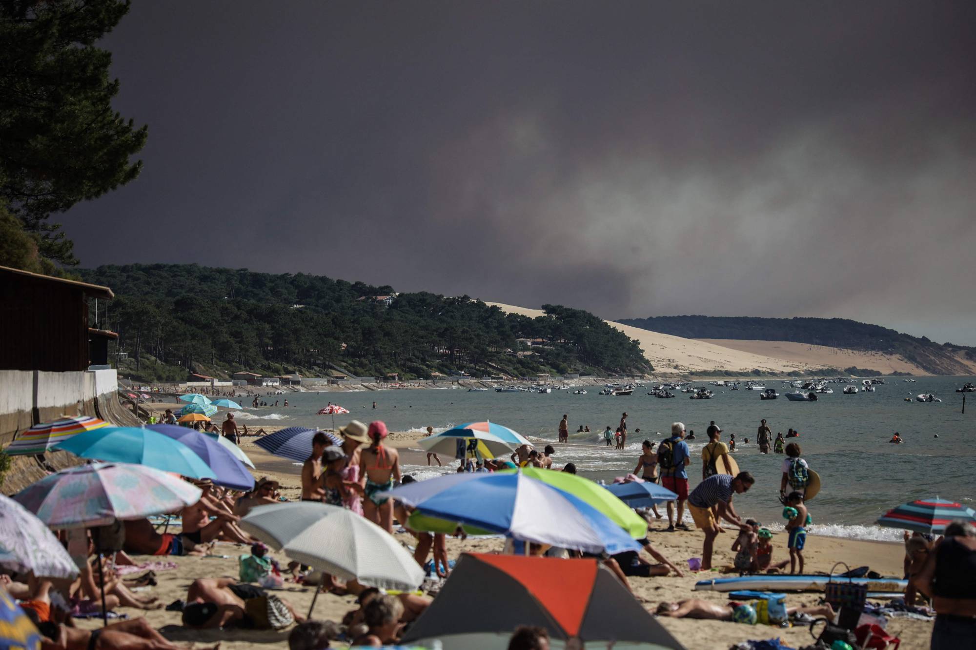 Beach-goers watch as a black cloud of smoke from a fire that hit La Teste-de-Buch forest rises from the Pyla Dune in the background, in the Arcachon basin in France on Wednesday. | AFP-JIJI