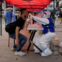 A medical worker collects a swab from a resident at a nucleic acid testing site amid a heatwave warning and a COVID-19 outbreak in Shanghai on Tuesday. | REUTERS