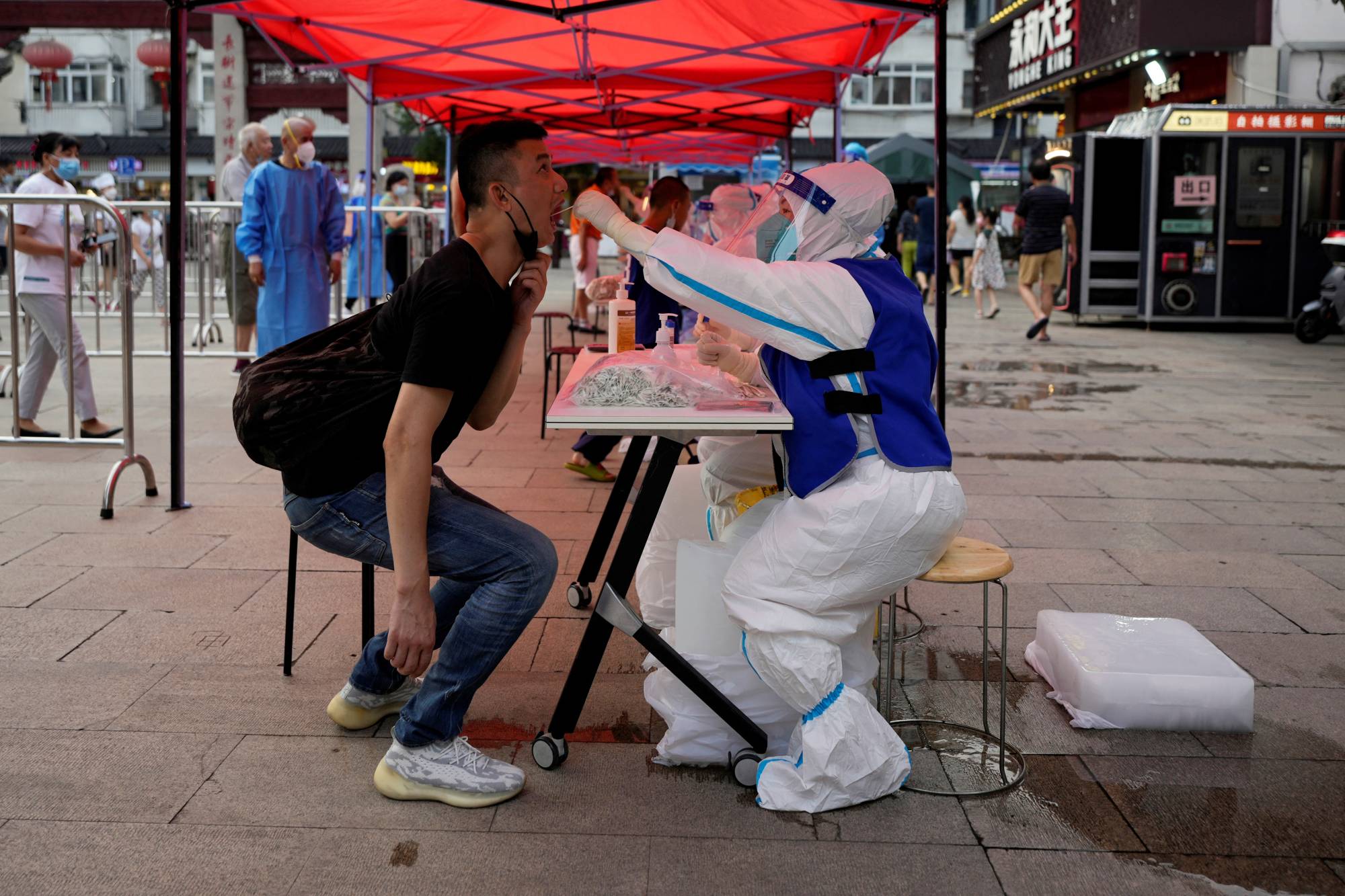 A medical worker collects a swab from a resident at a nucleic acid testing site amid a heatwave warning and a COVID-19 outbreak in Shanghai on Tuesday. | REUTERS