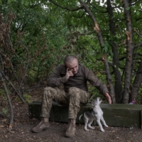 A Ukrainian soldier plays with a puppy as he speaks on his phone near the front lines in the Donetsk region of eastern Ukraine on Thursday. | MAURICIO LIMA / THE NEW YORK TIMES