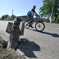 A cyclist rides past a tail section of a rocket embedded in a road in Kramatorsk, Ukraine, on July 4. A section in Japan\'s latest defense white paper noted that Japan “needs to closely monitor related developments with grave concern.” | AFP-JIJI