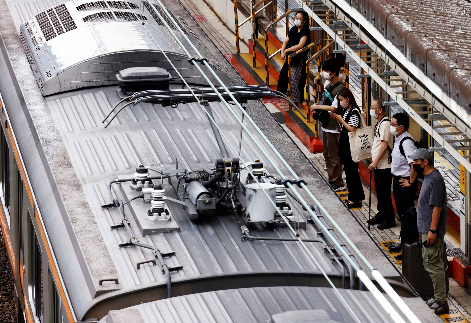 Passengers wait for a train at a station in Tokyo on Thursday. After a lull in new cases in the spring, the nation has seen a quick resurgence in COVID-19 infections over the past couple of weeks, driven by the highly contagious BA.5 omicron subvariant. | REUTERS