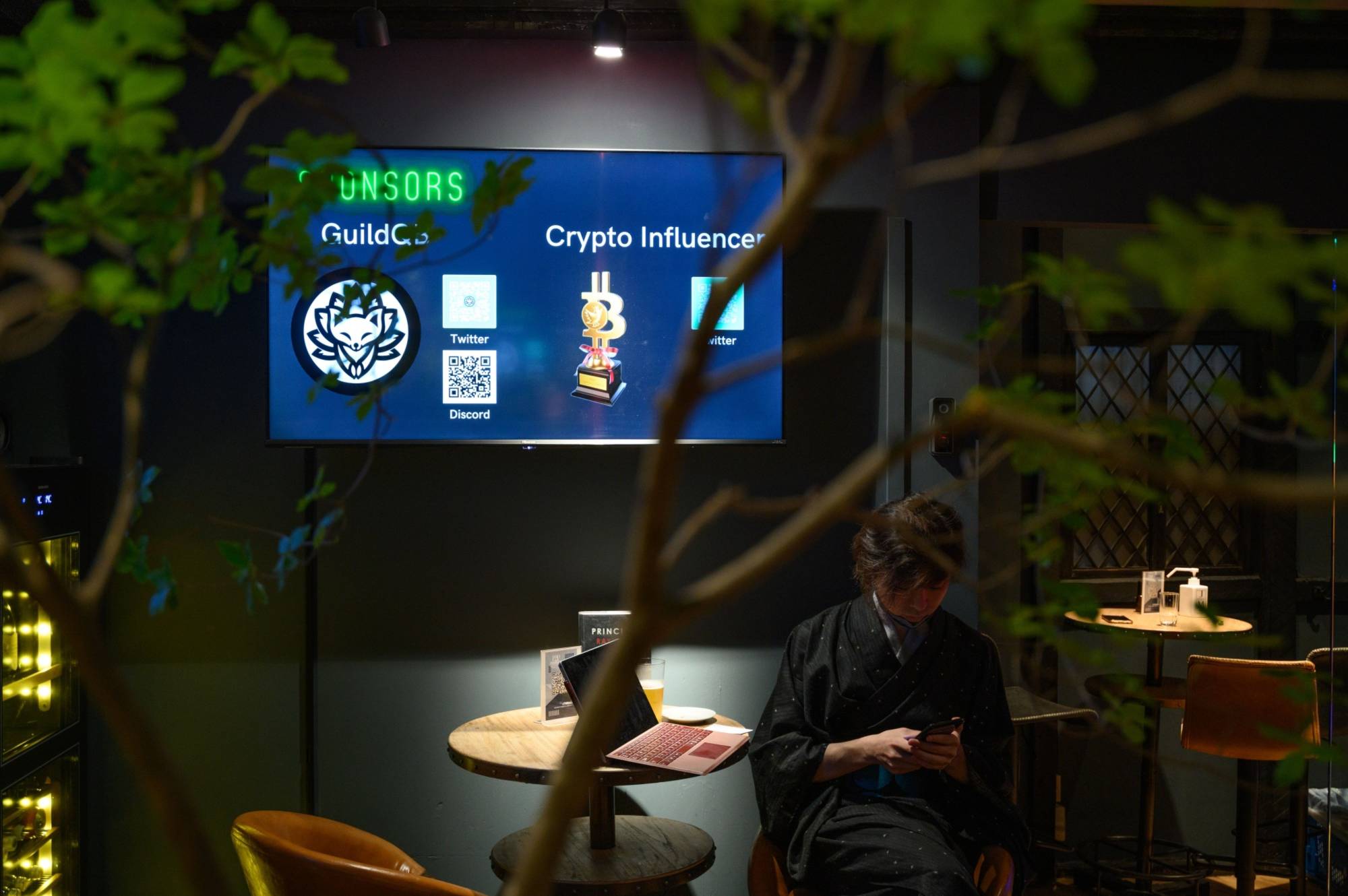 The logos of GuildQB and Crypto Influencer are displayed at CryptoBar P2P in Tokyo's Ginza district in June. Cryptocurrency lobbying groups in Japan plan to ask the government to ease corporate tax rules that are seen to be stunting growth of the local digital asset industry. | BLOOMBERG