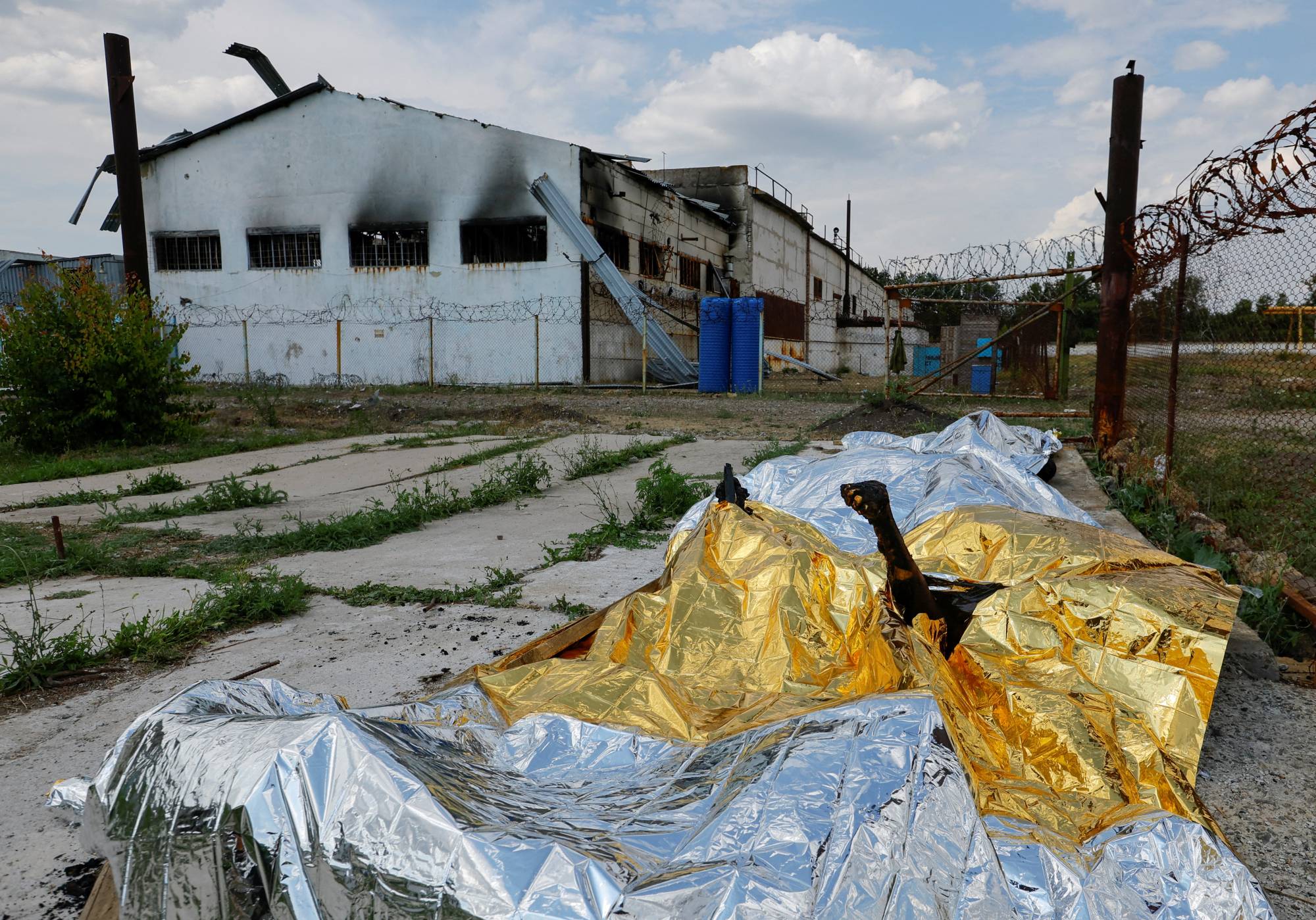 Burnt bodies of detainees lie covered following the shelling at a pre-trial detention center in Olenivka, Ukraine, on Friday.  | REUTERS