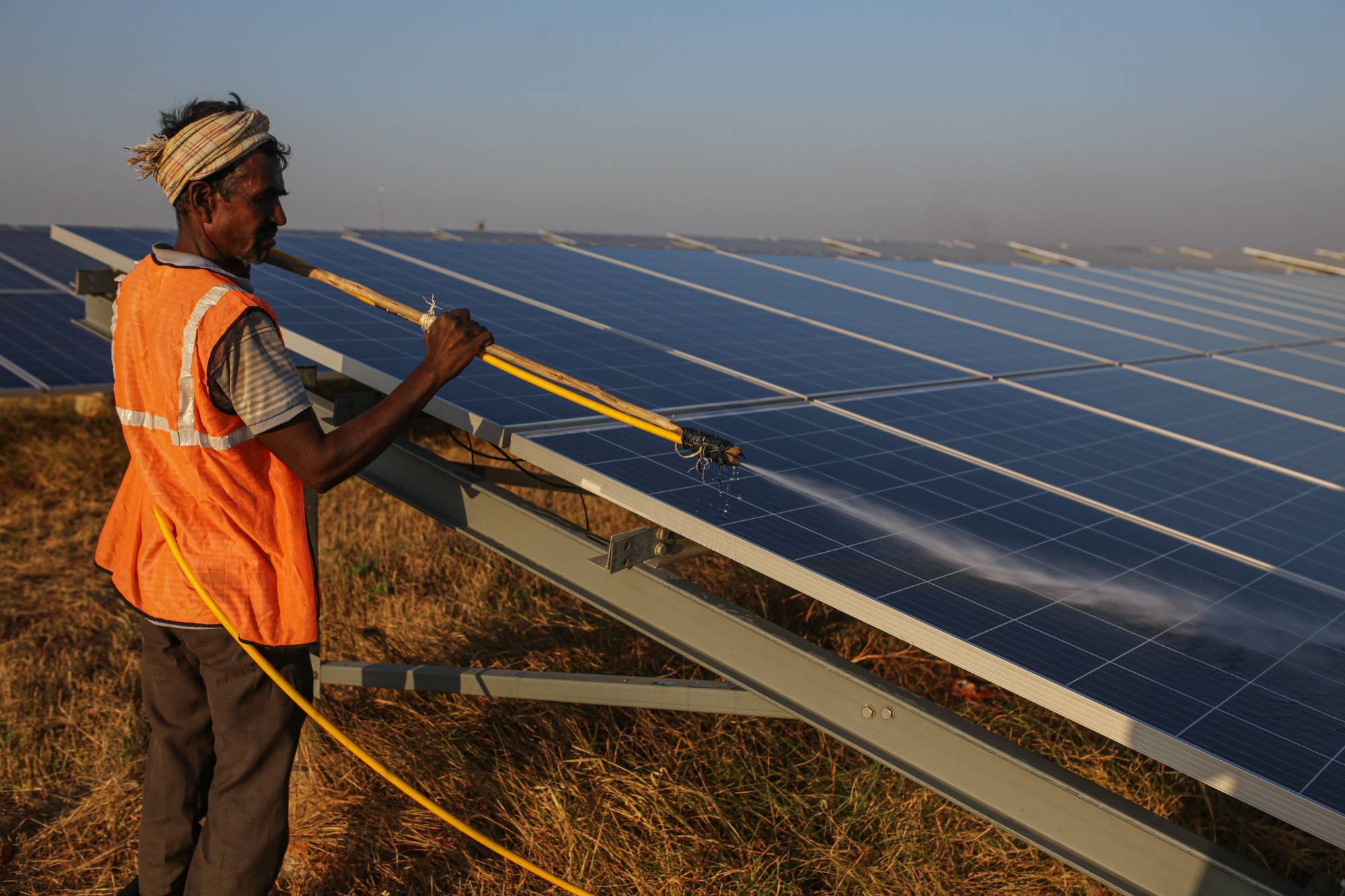 A worker washes photovoltaic panels at a solar farm in Pavagada, Karnataka, India, in February. | Bloomberg
