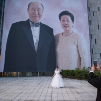 A bride poses for a photo before a giant image of the late Rev. Sun Myung Moon and his wife, Hak Ja Han Moon, before a mass wedding ceremony held by the Unification Church in Gapyeong, South Korea, in 2017. | AFP-JIJI