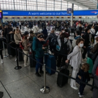 Passengers wait to check in at British Airways desks inside the departures hall of Terminal 5 at Heathrow Airport in London in April. | BLOOMBERG