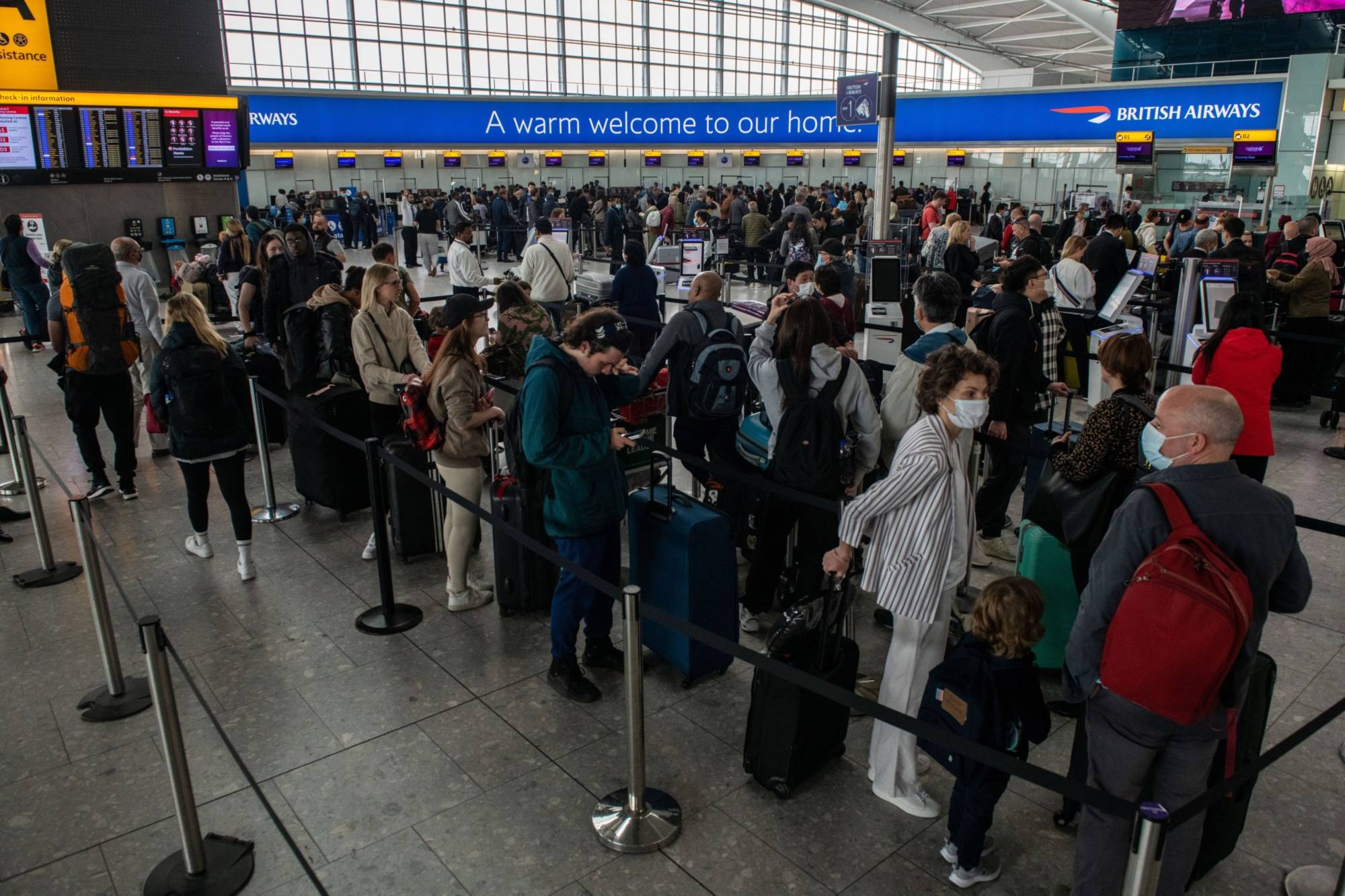 Passengers wait to check in at British Airways desks inside the departures hall of Terminal 5 at Heathrow Airport in London in April. | Bloomberg