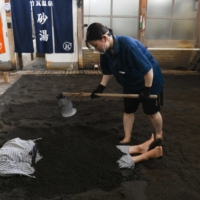 A worker covers a customer with sand at Takegawara Onsen, a hot-spring facility in Beppu, Oita Prefecture, on July 27. | BLOOMBERG