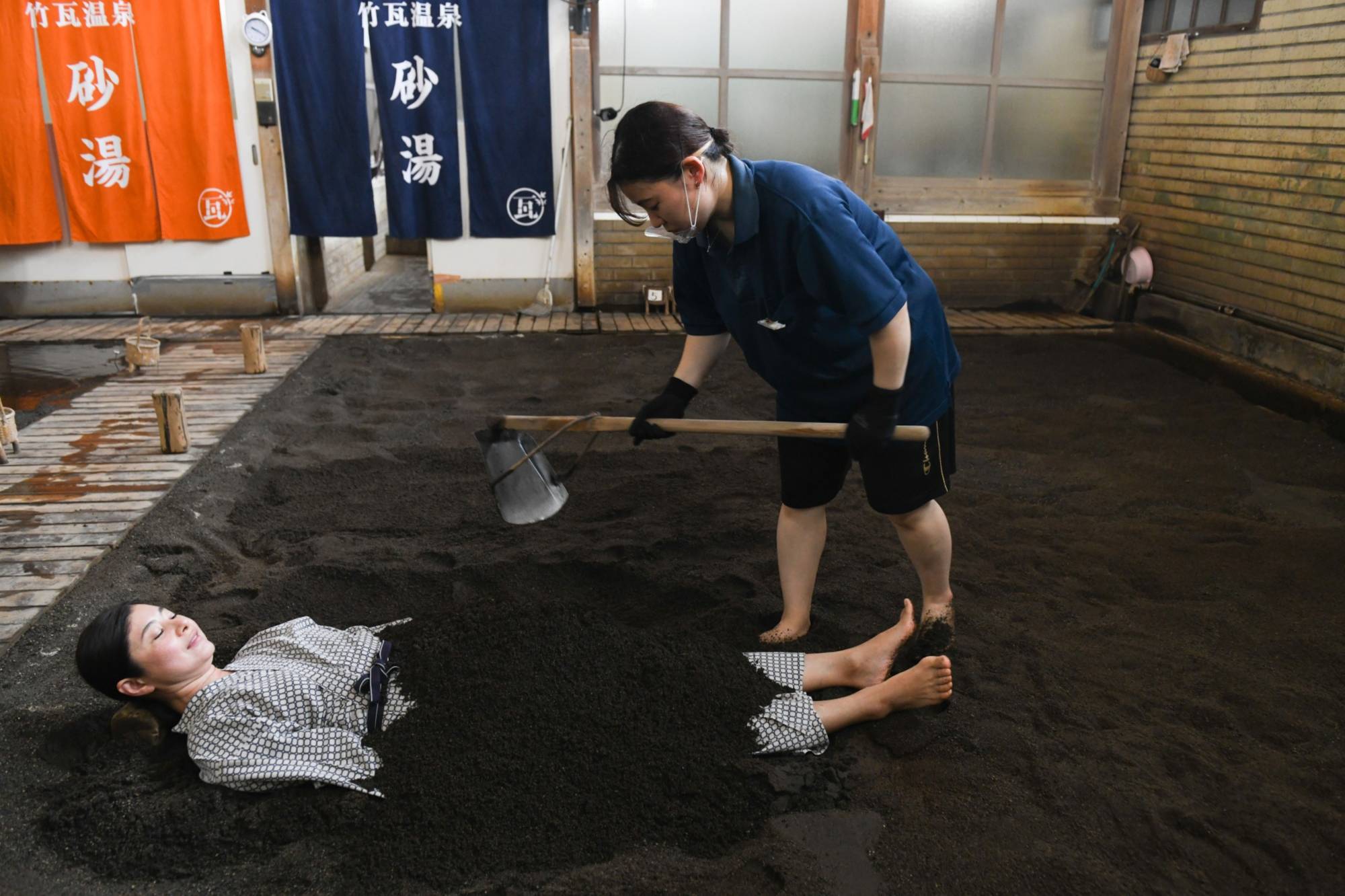 A worker covers a customer with sand at Takegawara Onsen, a hot-spring facility in Beppu, Oita Prefecture, on July 27. | Bloomberg
