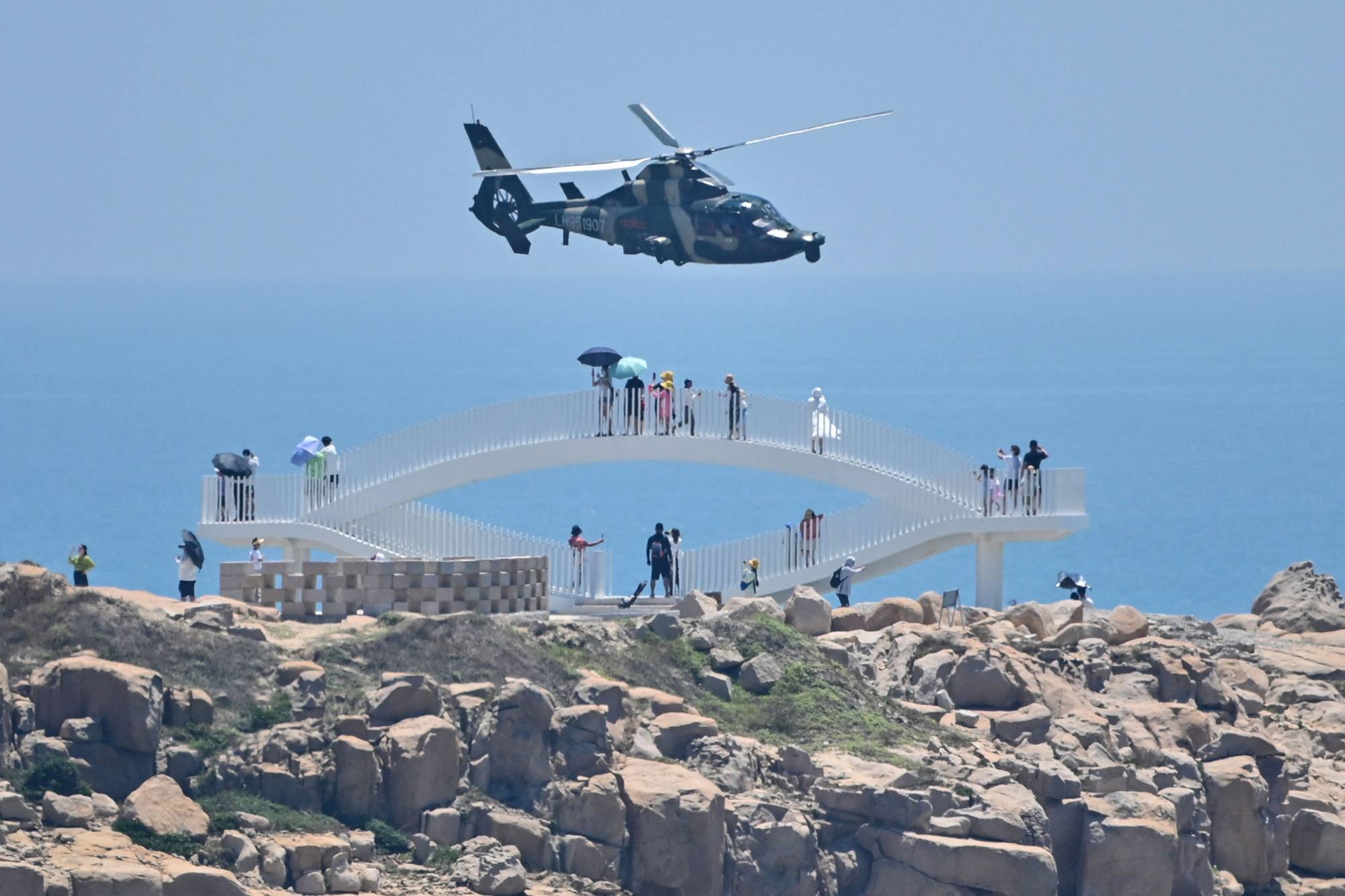 Tourists look on as a Chinese military helicopter flies past Pingtan island, one of mainland China's closest points to Taiwan, in Fujian province on Thursday, ahead of massive military drills off Taiwan. | AFP-JIJI