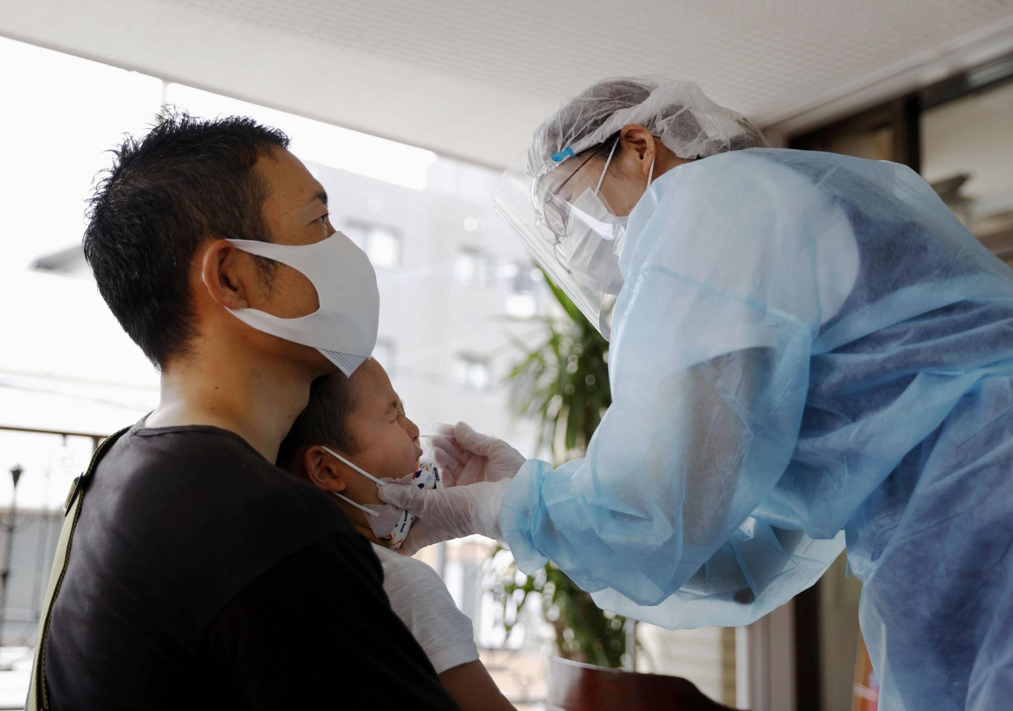 A nurse tests a child for COVID-19 at a makeshift 'fever clinic' outside a pediatric clinic in Fukuoka on Thursday. | KYODO