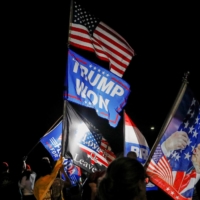 Supporters of former U.S. President Donald Trump wave flags as they gather outside his Mar-a-Lago home after Trump said that FBI agents raided it, in Palm Beach, Florida, on Monday. | REUTERS