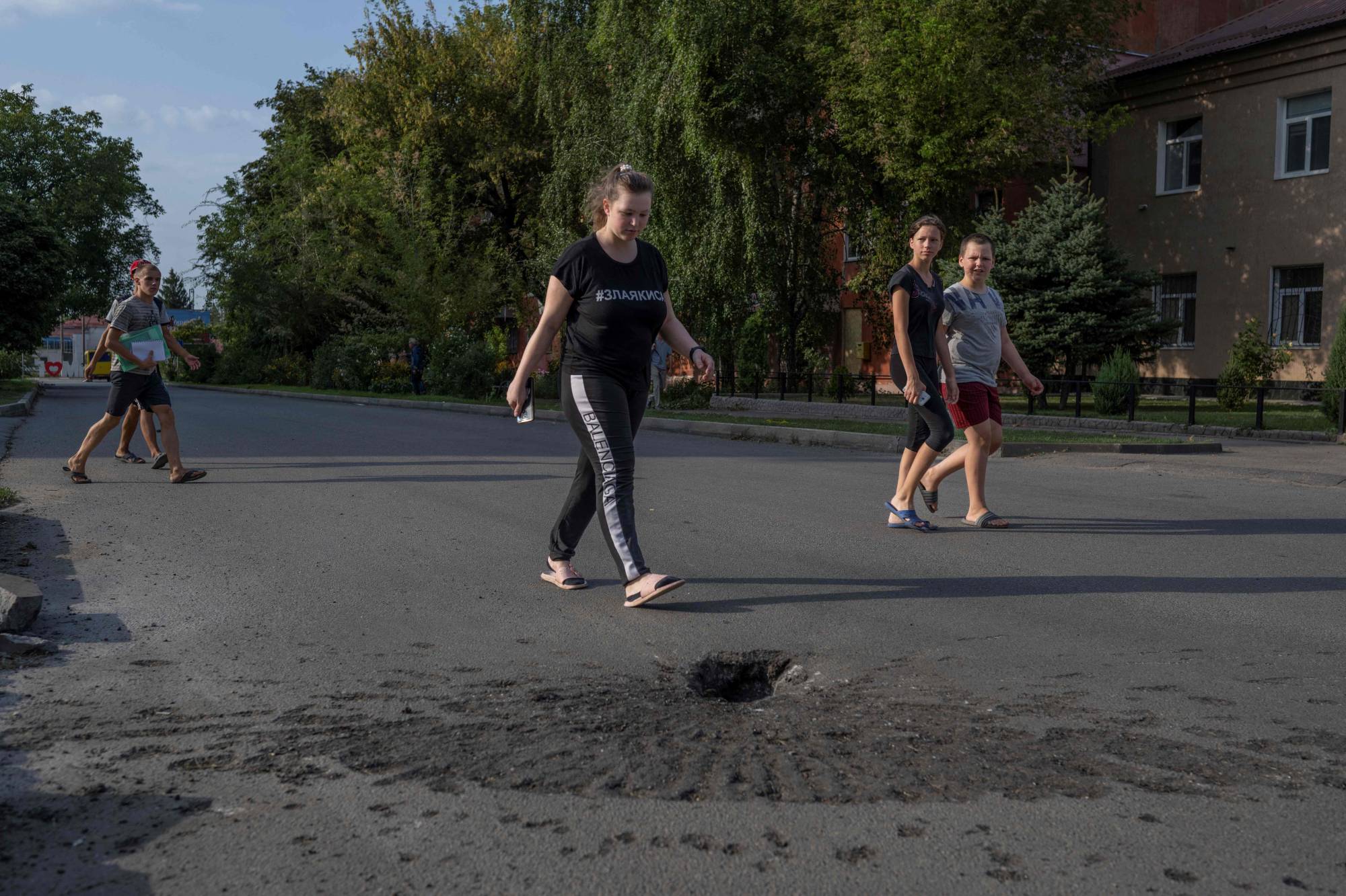 People walk next to a crater left by shelling from Russian forces in Marhanets, Ukraine. | AFP-JIJI