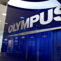 A man sits near the Olympus Corp logo at company headquarters in Tokyo. | REUTERS