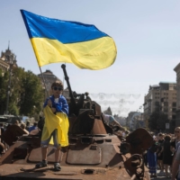 A boy waves a Ukrainian national flag atop an armored personal carrier Sunday in Kyiv at an exhibition of destroyed Russian military vehicles and weapons in the capital, ahead of the country\'s Independence Day on Wednesday. | REUTERS