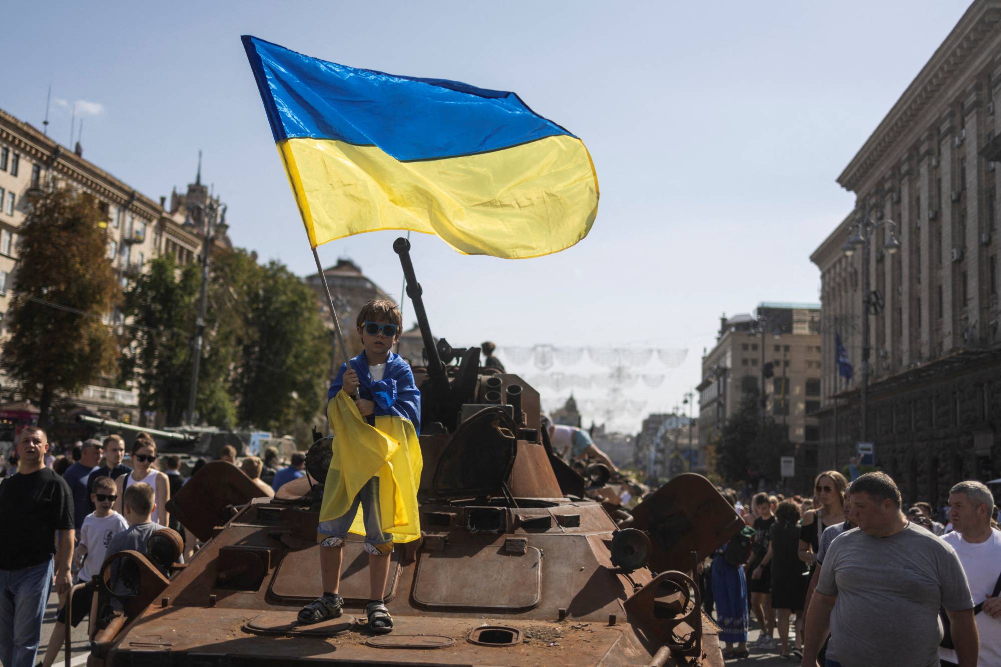 A boy waves a Ukrainian national flag atop an armored personal carrier Sunday in Kyiv at an exhibition of destroyed Russian military vehicles and weapons in the capital, ahead of the country's Independence Day on Wednesday. | REUTERS
