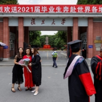 Students take graduation photos in front of a statue of Chinese leader Mao Zedong and a signboard marking the 100th anniversary of the founding of the Communist Party of China, at Fudan University in Shanghai in June last year. | REUTERS