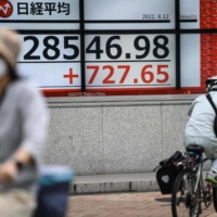 People cycle past a board showing the closing numbers of the Tokyo Stock Exchange in Tokyo on Aug. 12. | AFP-JIJI