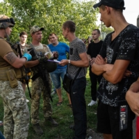 Ukrainian soldiers check the paperwork of men arriving from Kherson to the Ukrainian controlled checkpoint in Novooleksandrivka, outside of Zaporizhzhia, Ukraine, on Sunday. | LYNSEY ADDARIO / THE NEW YORK TIMES