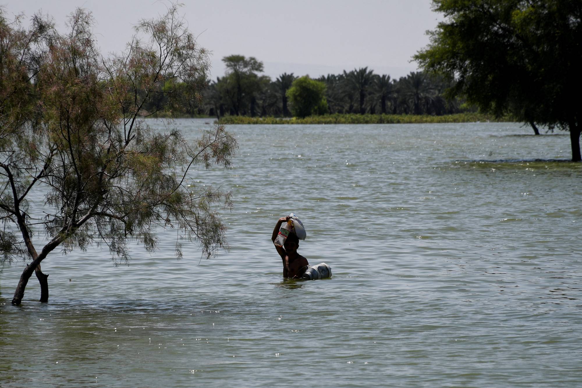 A flood victim wades through flood water following rains and floods during the monsoon season in Sehwan, Pakistan, on Wednesday. | REUTERS