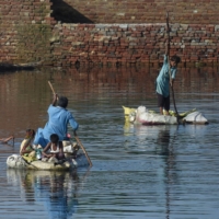 People use rafts to cross a flooded area after monsoon rains on the outskirts of Sukkur, Sindh province, Pakistan, on Thursday. | AFP-JIJI
