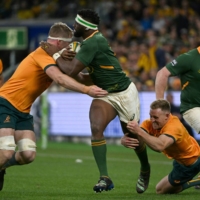 South Africa\'s Siya Kolisi (center) attempts to break away from Australia\'s Matt Philip (left) and Reece Hodge during their Rugby Championship match against Australia in Sydney on Saturday. | AFP-JIJI
