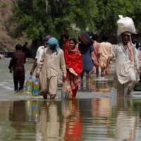 Residents walk amid flood water as they head to their villages, following rains and floods during the monsoon season in Sehwan, Pakistan, on Tuesday. | REUTERS