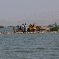 A woman and children walk along a road damaged by flooding in Bajara village, at the banks of Manchar lake, in Sehwan, Pakistan, on Tuesday. | REUTERS