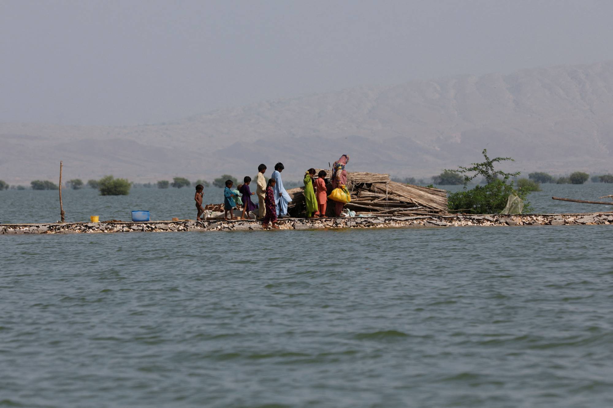 A woman and children walk along a road damaged by flooding in Bajara village, at the banks of Manchar lake, in Sehwan, Pakistan, on Tuesday. | REUTERS