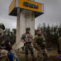 Ukrainian military personnel pose by the landmark sign outside of Izium on Wednesday. | NICOLE TUNG / THE NEW YORK TIMES