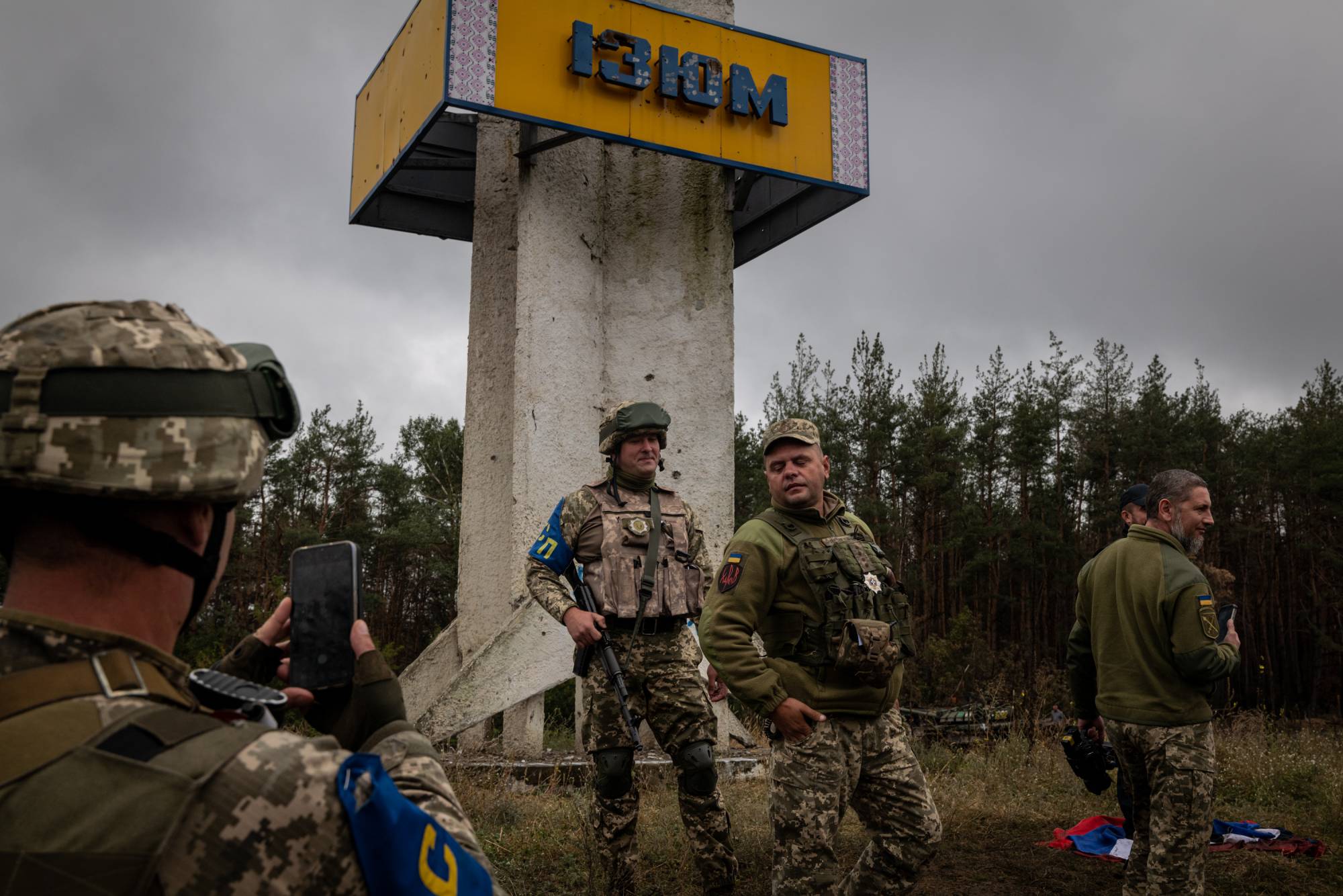 Ukrainian military personnel pose by the landmark sign outside of Izium on Wednesday. | Nicole Tung / The New York Times