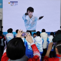 Volunteers at the main media center watch Yuzuru Hanyu perform during the 2022 Beijing Winter Games on Feb. 10. | REUTERS