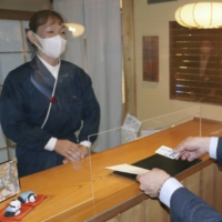 A customer checks in at an inn in Kyoto. The government is considering allowing hotels and inns to refuse guests who do not wear masks. | KYODO

