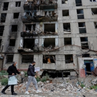 Members of an electoral commission walk past a destroyed building with a mobile ballot box and documents while visiting local residents on the second day of a referendum on the joining of the self-proclaimed Donetsk People\'s Republic to Russia, in Mariupol, Ukraine, on Saturday.  | REUTERS
