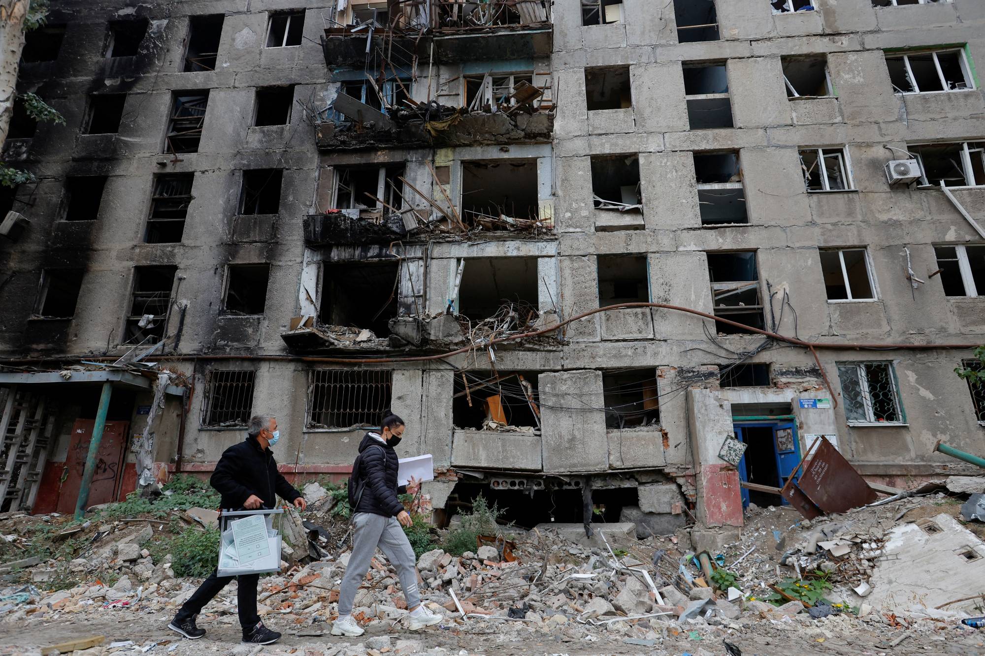 Members of an electoral commission walk past a destroyed building with a mobile ballot box and documents while visiting local residents on the second day of a referendum on the joining of the self-proclaimed Donetsk People's Republic to Russia, in Mariupol, Ukraine, on Saturday. | Reuters