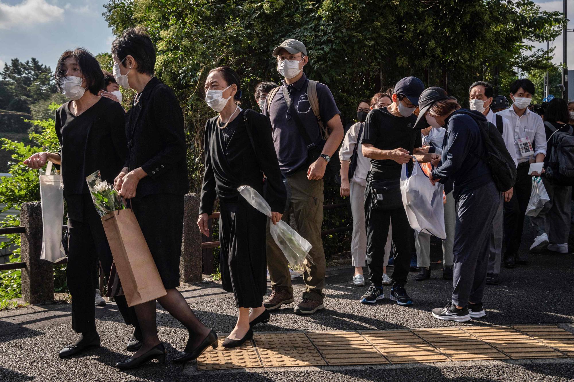 People line up along a street near Nippon Budokan to leave flowers and sign a condolence book ahead of the state funeral for former Prime Minister Shinzo Abe. | AFP-JIJI