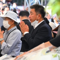 People pray as they leave flowers in memory of former Prime Minister Shinzo Abe. | AFP-JIJI