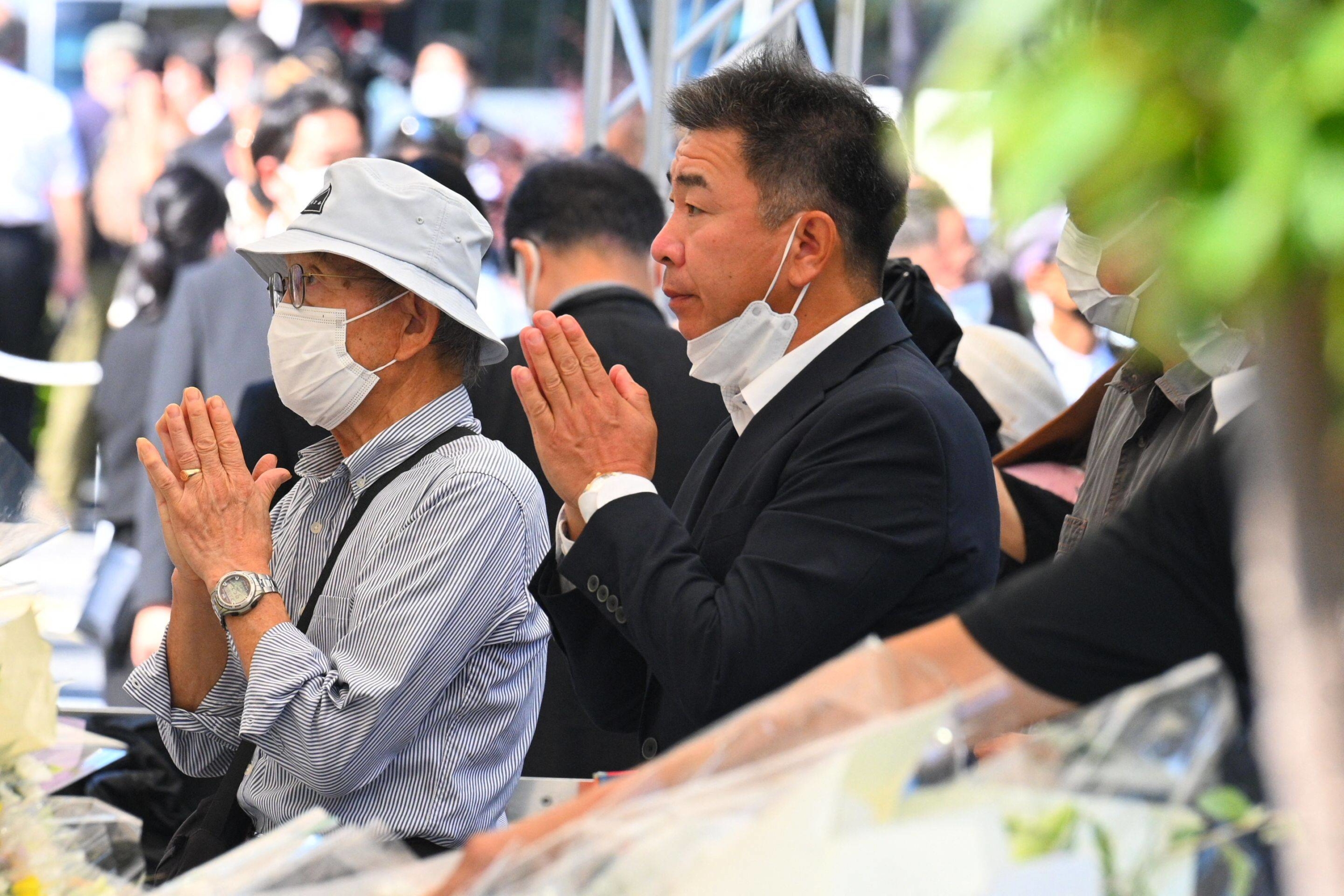 People pray as they leave flowers in memory of former Prime Minister Shinzo Abe. | AFP-JIJI