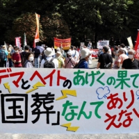 Protesters carrying a banner protesting the state funeral | AFP-JIJI