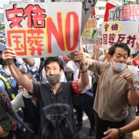 Protesters carrying placards rally against the state funeral. | AFP-JIJI