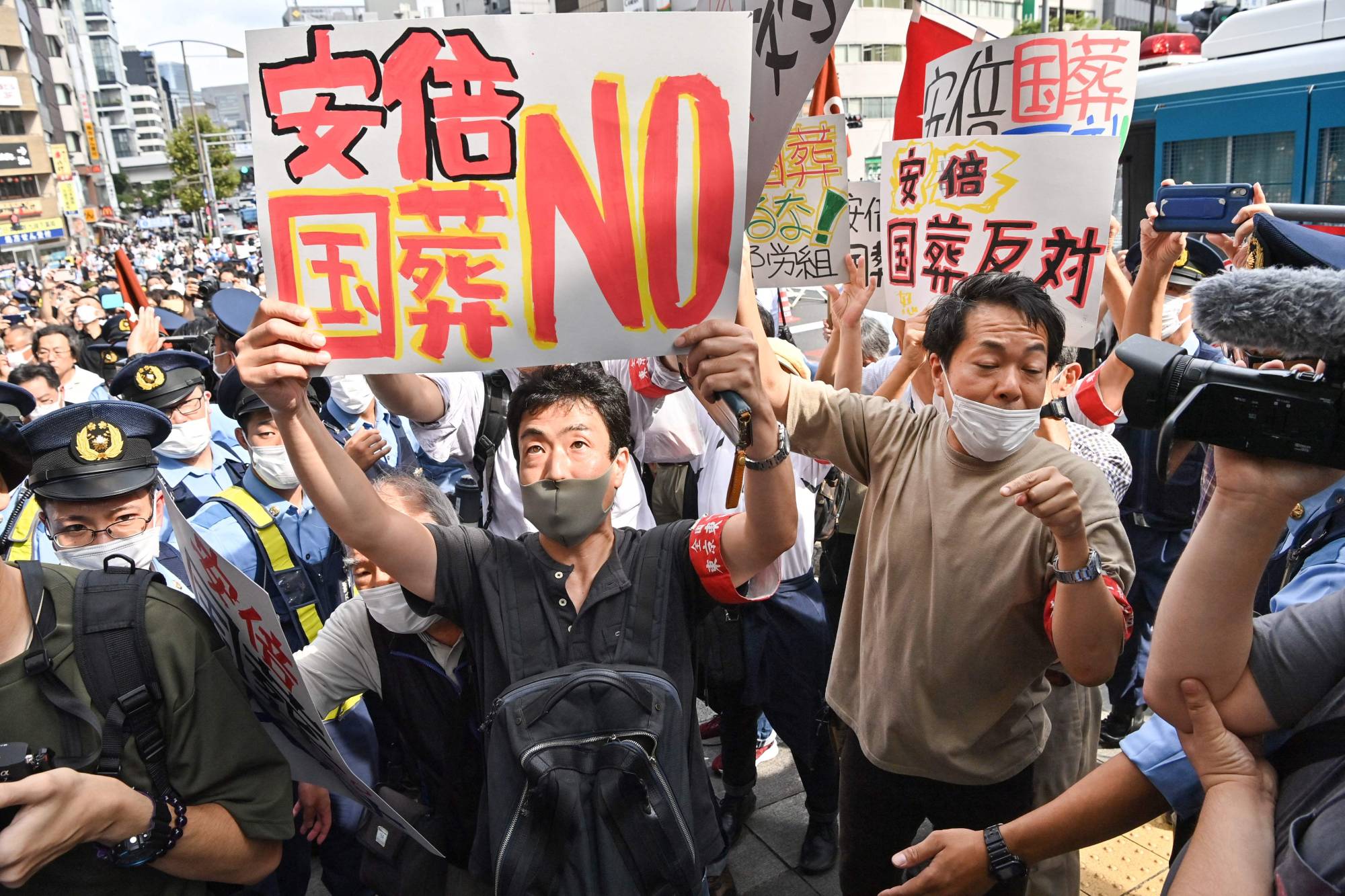 Protesters carrying placards rally against the state funeral. | AFP-JIJI