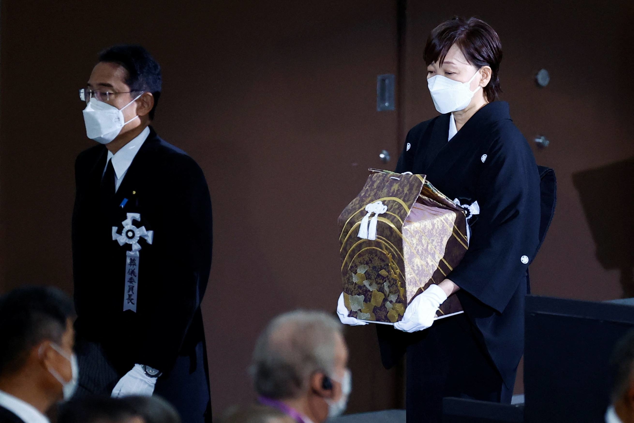 Akie Abe carries the urn containing her husband's ashes, as she walks behind Prime Minister Fumio Kishida. | POOL / VIA REUTERS