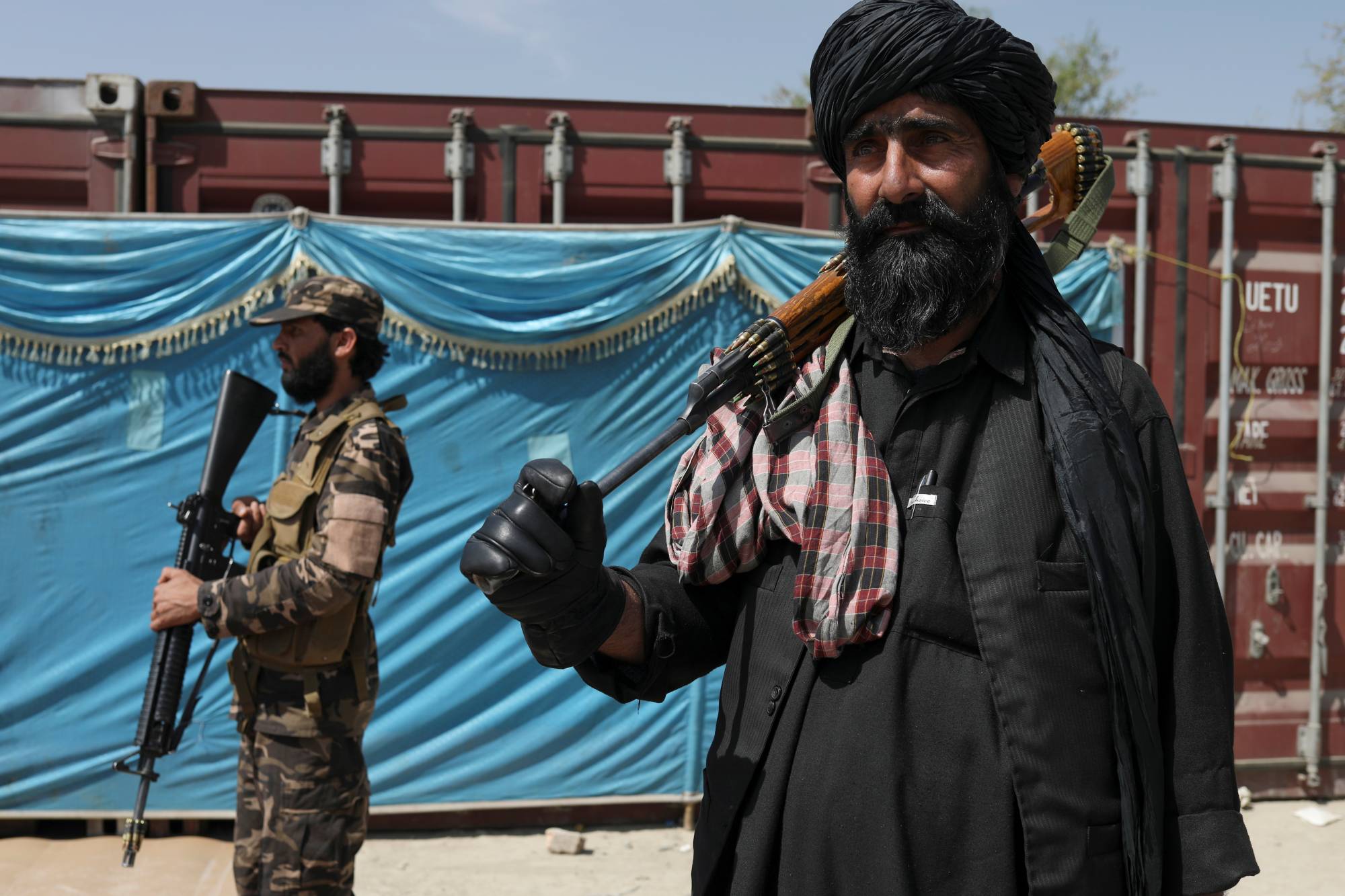 Taliban fighters stand guard while people wait to receive sacks of rice as part of humanitarian aid sent by China to Afghanistan, at a distribution center in Kabul on April 7. | REUTERS