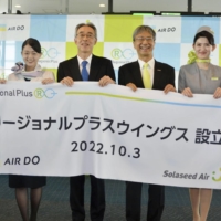 Air Do President Susumu Kusano (center left) and Solaseed Air President Kosuke Takahashi (center right) attend a ceremony at Haneda Airport on Monday as the two regional airlines merged their operations. | KYODO
