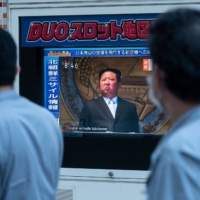 People walk past a public television screen in Tokyo on Oct. 4, displaying file footage of North Korean leader Kim Jong Un. | AFP-JIJI