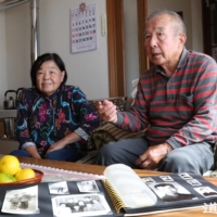 Kohei Yamada (right) and his wife, Keiko, in the town of Atsuma, Hokkaido, with family photos taken in China | HOKKAIDO SHIMBUN
