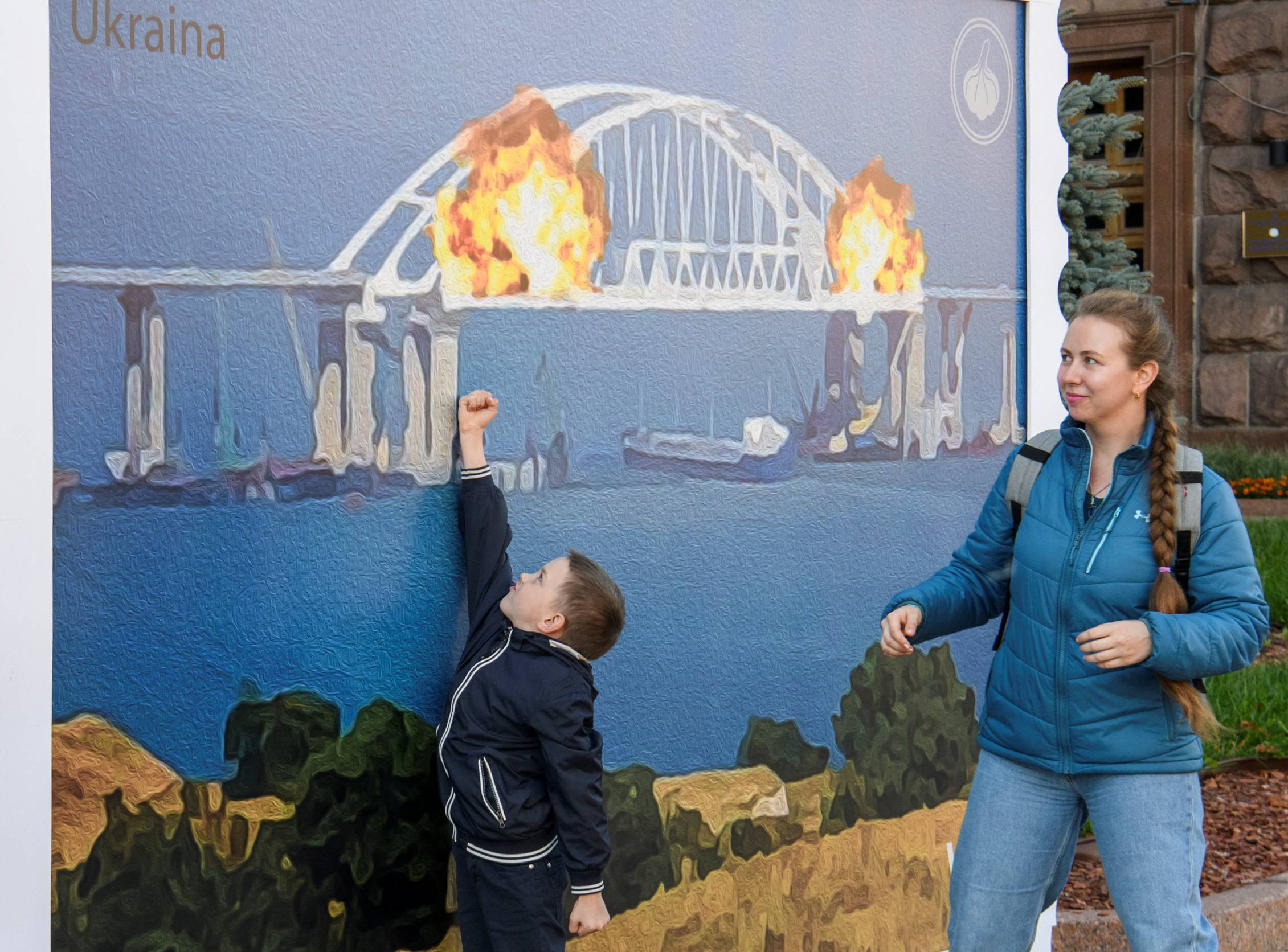 Ukrainians in Kyiv on Saturday pose in front of artwork depicting the Kerch bridge on fire.  | REUTERS