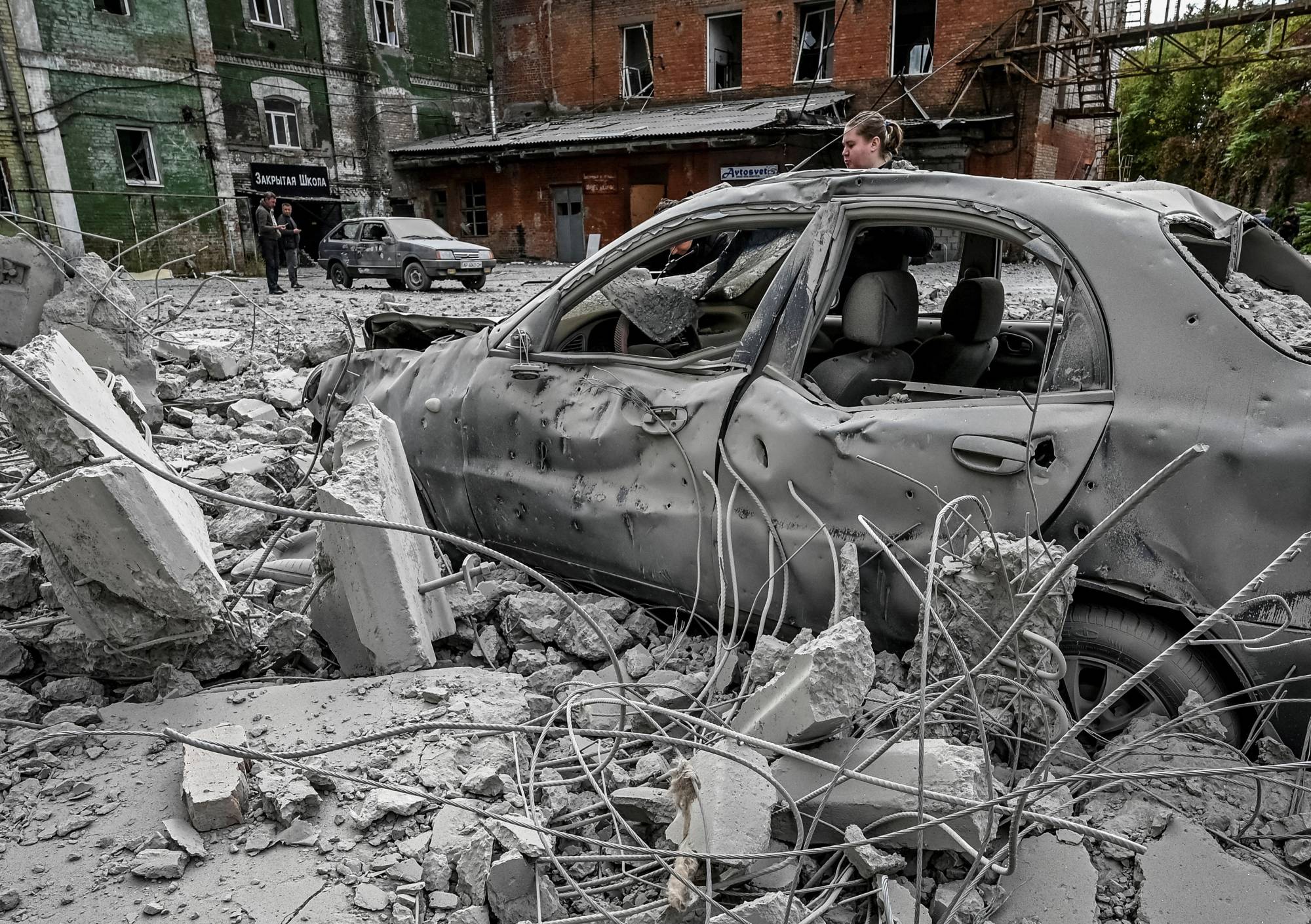 A woman stands near her car, which was destroyed by a Russian missile attack, in Zaporizhzhia, Ukraine, on Friday. | Reuters